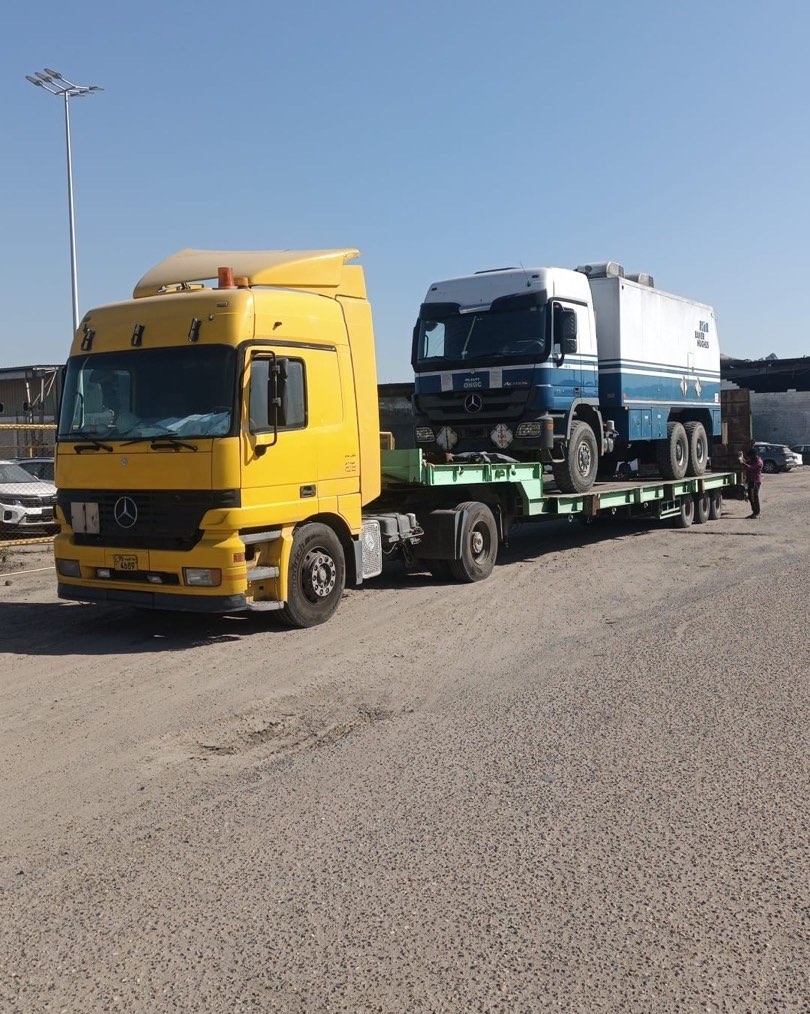 Yellow Mercedes low-bed carrying a blue-white Mercedes truck at port