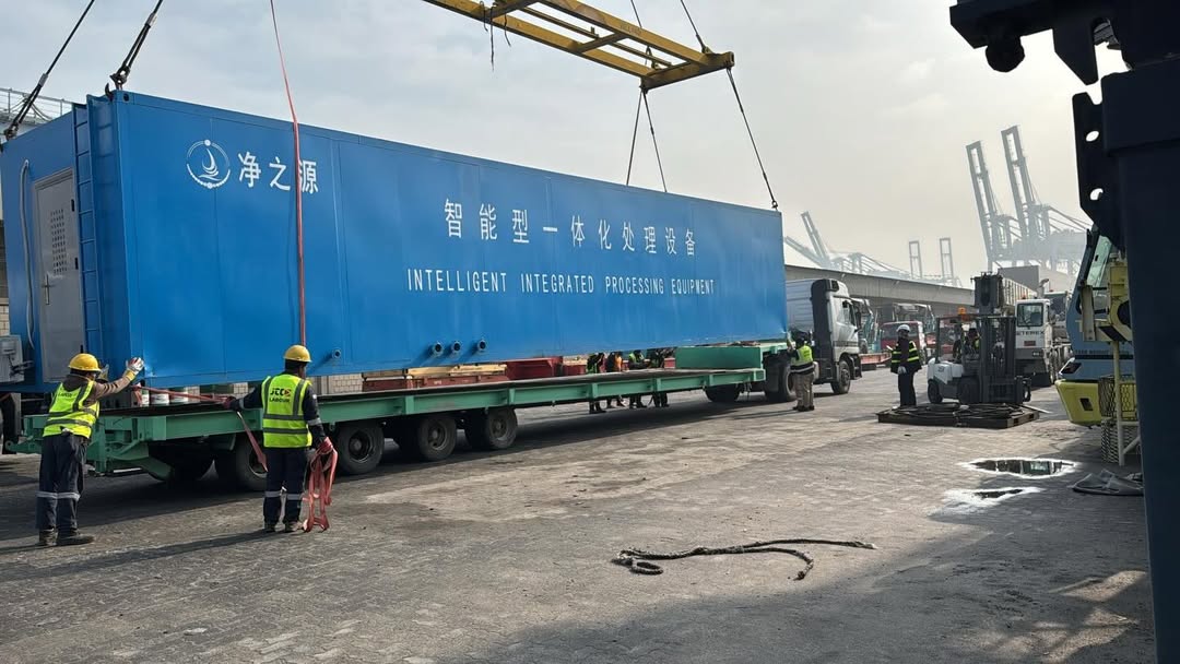 Two JLG boom lifts loaded on low-bed trailer at warehouse